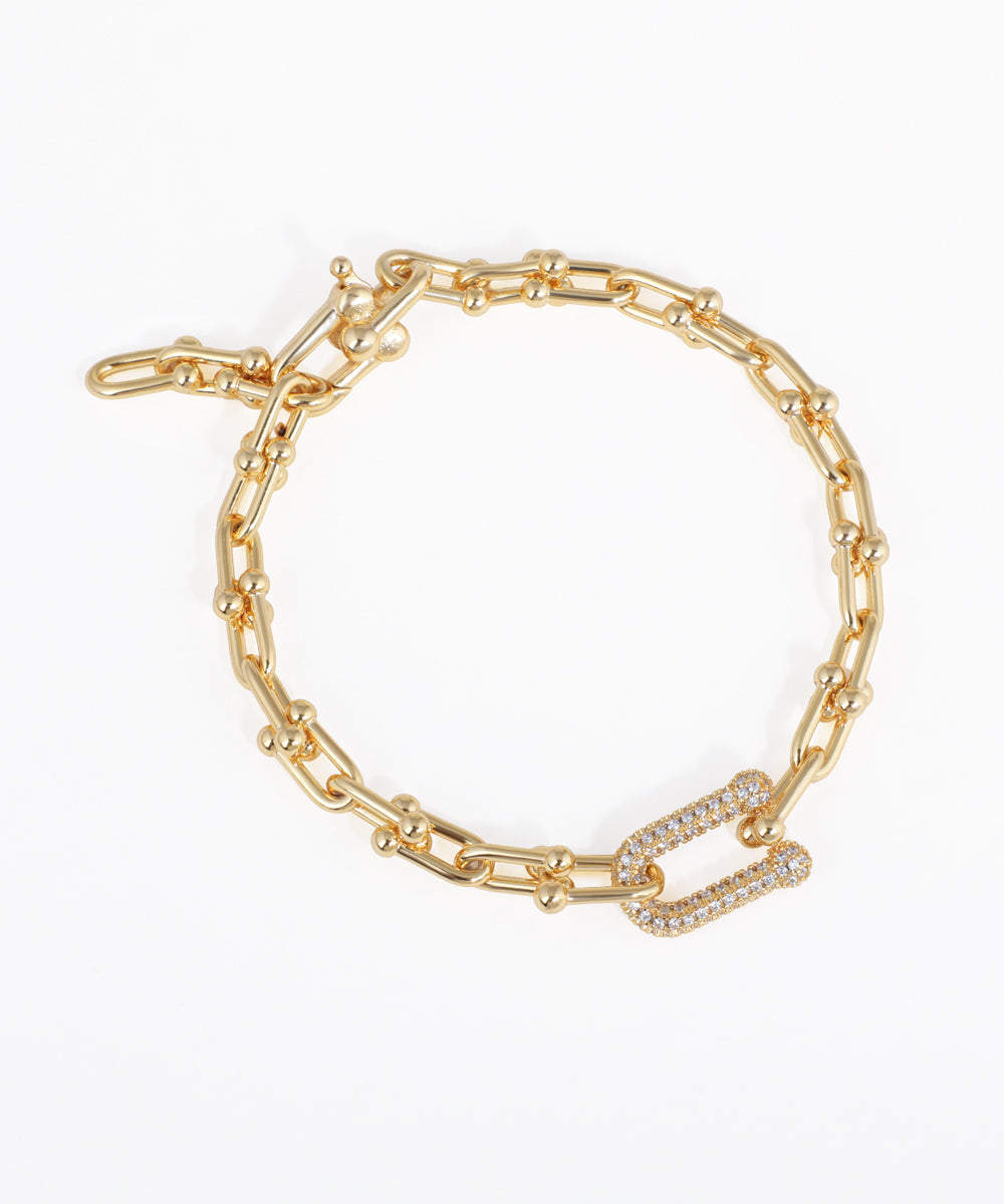 Gold-tone chain link bracelet with textured links and a U-shaped clasp encrusted with clear stones.