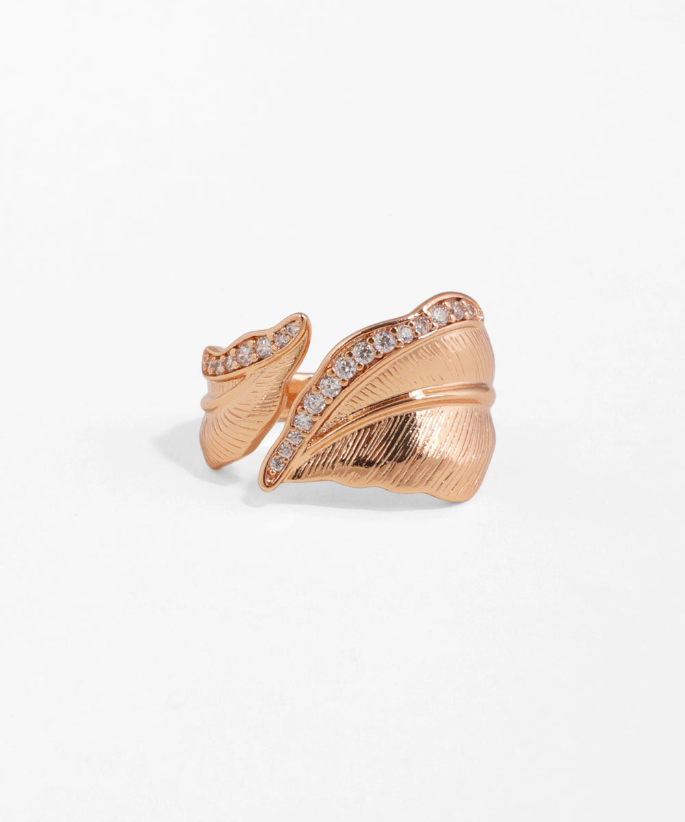 Rose gold leaf-shaped ring with embedded stones on a light gray background