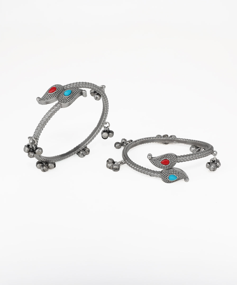 Pair of silver bangles with red and blue stones on a white background