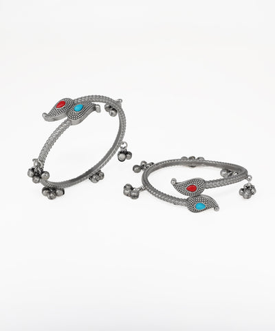 Pair of silver bangles with red and blue stones on a white background
