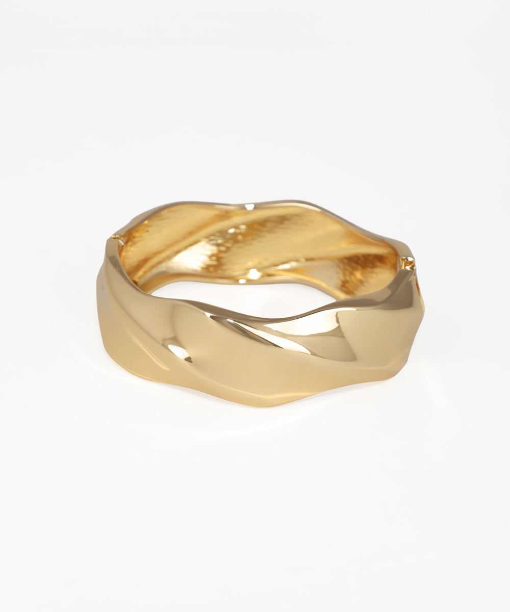 Gold-tone bangle kada with a wide, polished, wavy sculptural design and hinged closure