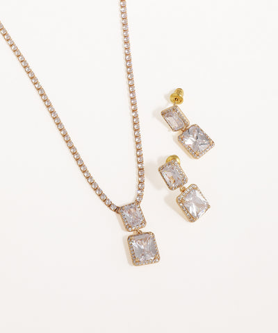 Gold necklace and earrings with clear gemstones on a white background