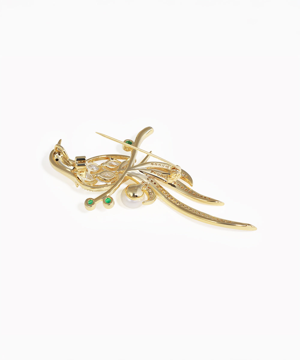 Gold brooch with pearls and emeralds on a white background