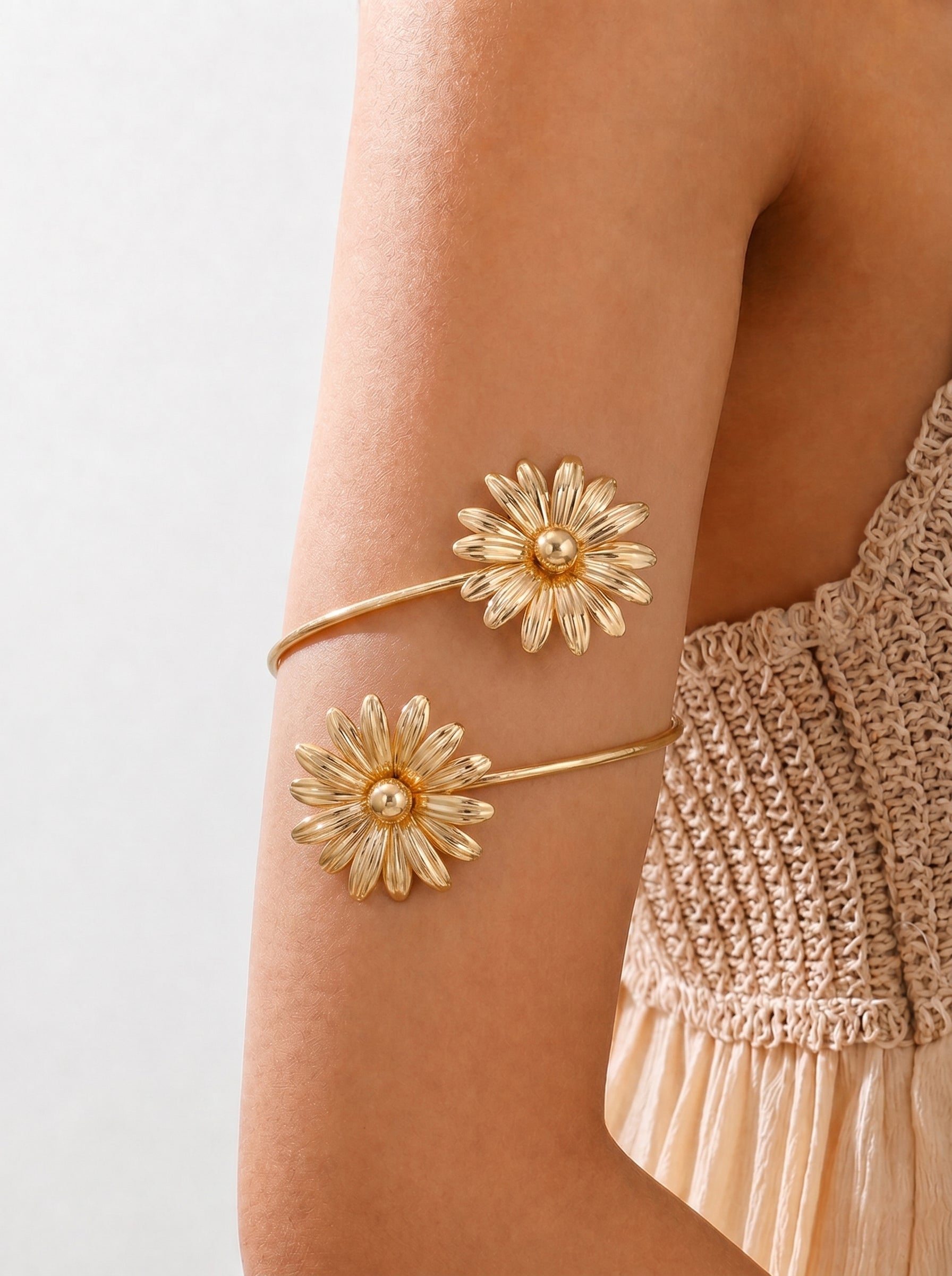 Gold floral arm cuffs on a person's arm with a neutral background
