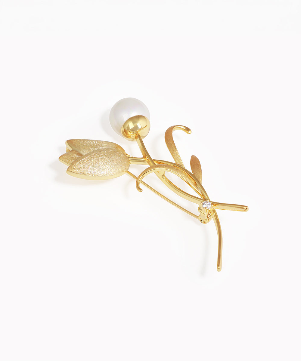 Gold-tone brooch with a sculpted tulip design, featuring a faux pearl bud, textured metal flower, and a clear stone.