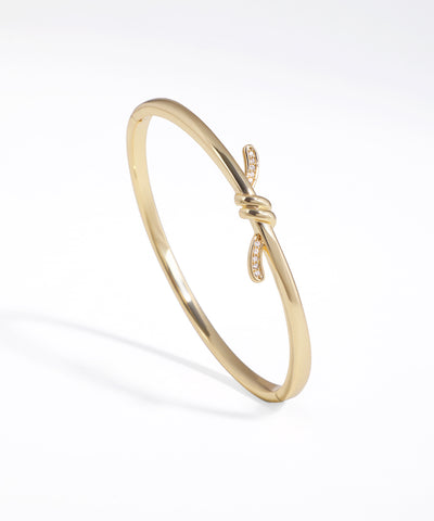 Gold-tone cuff bracelet with a central knot design embellished with clear CZ stones on a white background.