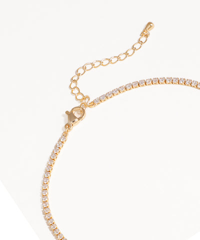 Gold bracelet with clear gemstones on a white background