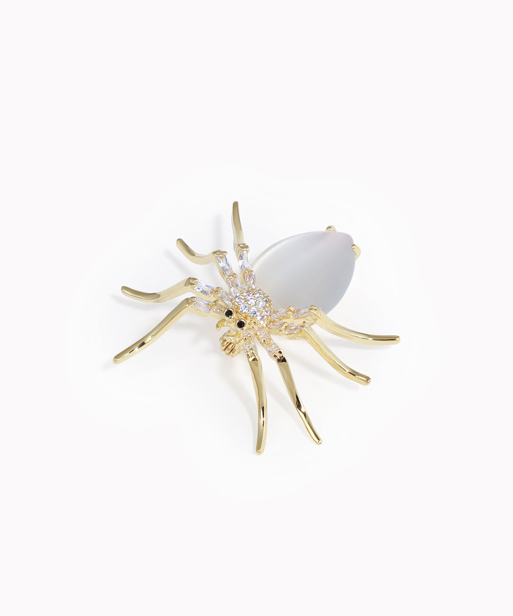Gold spider-shaped brooch with a white center on a white background