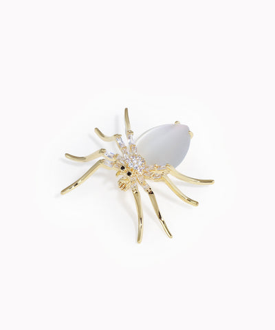 Gold spider-shaped brooch with a white center on a white background