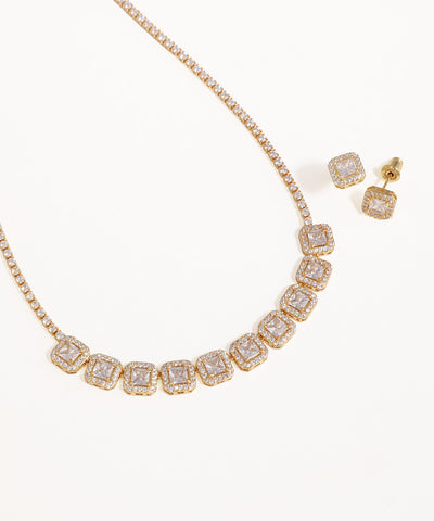 Gold necklace and earrings with clear gemstones on a white background