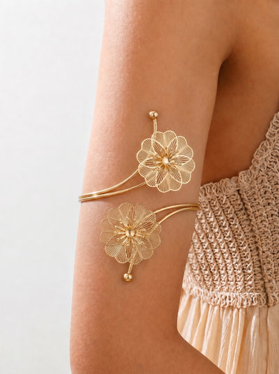 Gold floral arm cuffs on a person's arm with a neutral background
