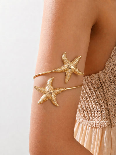 Gold starfish-shaped bangles on a person's arm with a neutral background