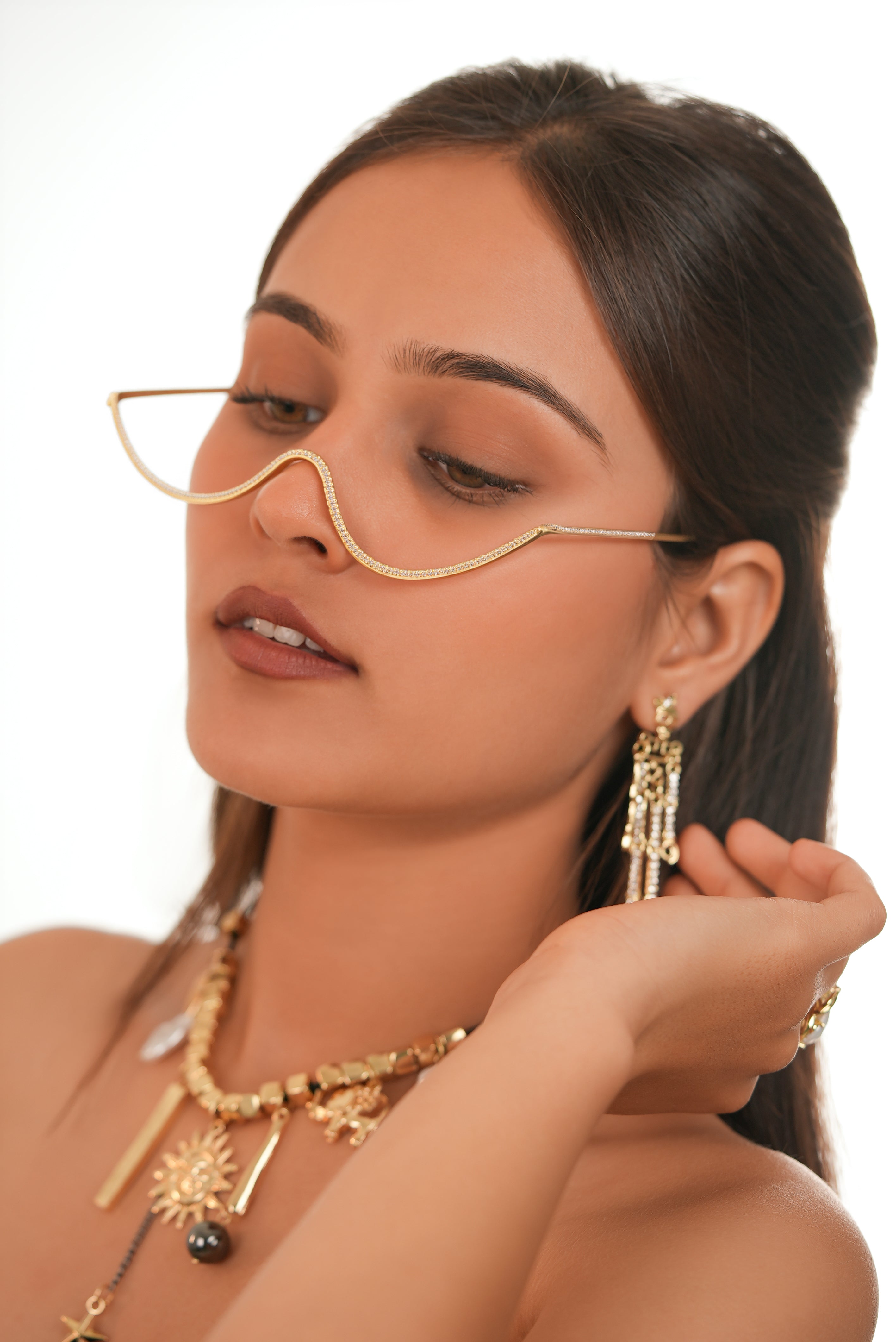 Woman wearing gold jewelry including earrings and a necklace, with a plain background