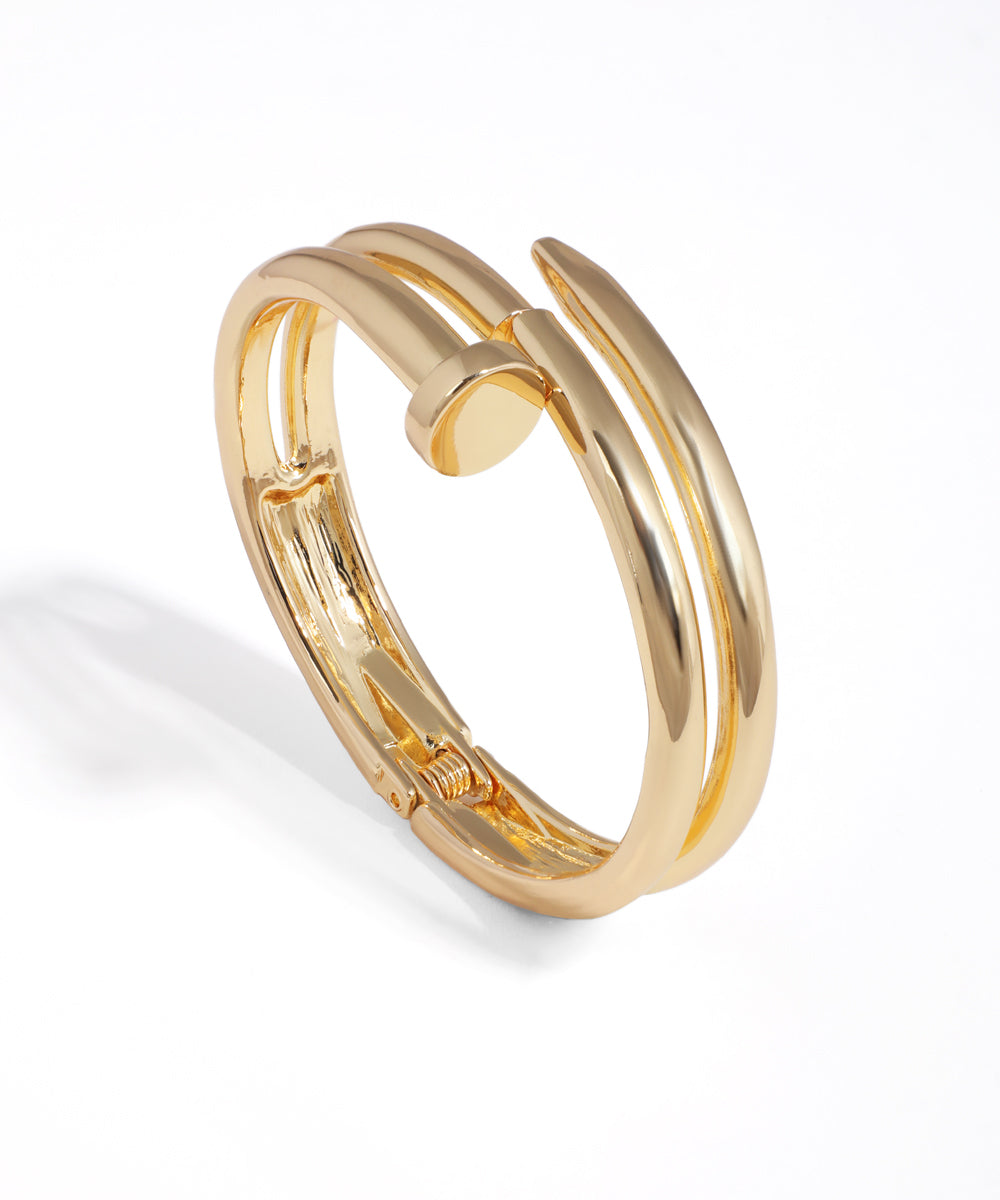 Gold-tone bangle bracelet with a distinctive nail-inspired design and hinged clasp closure.