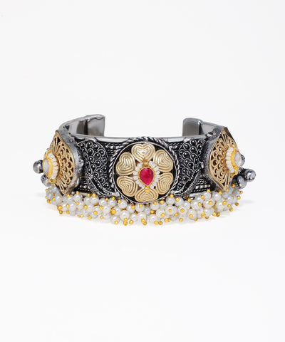 Decorative bracelet with intricate designs and a red gemstone on a white background