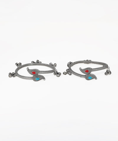 Pair of silver bangles with red and blue stones on a white background