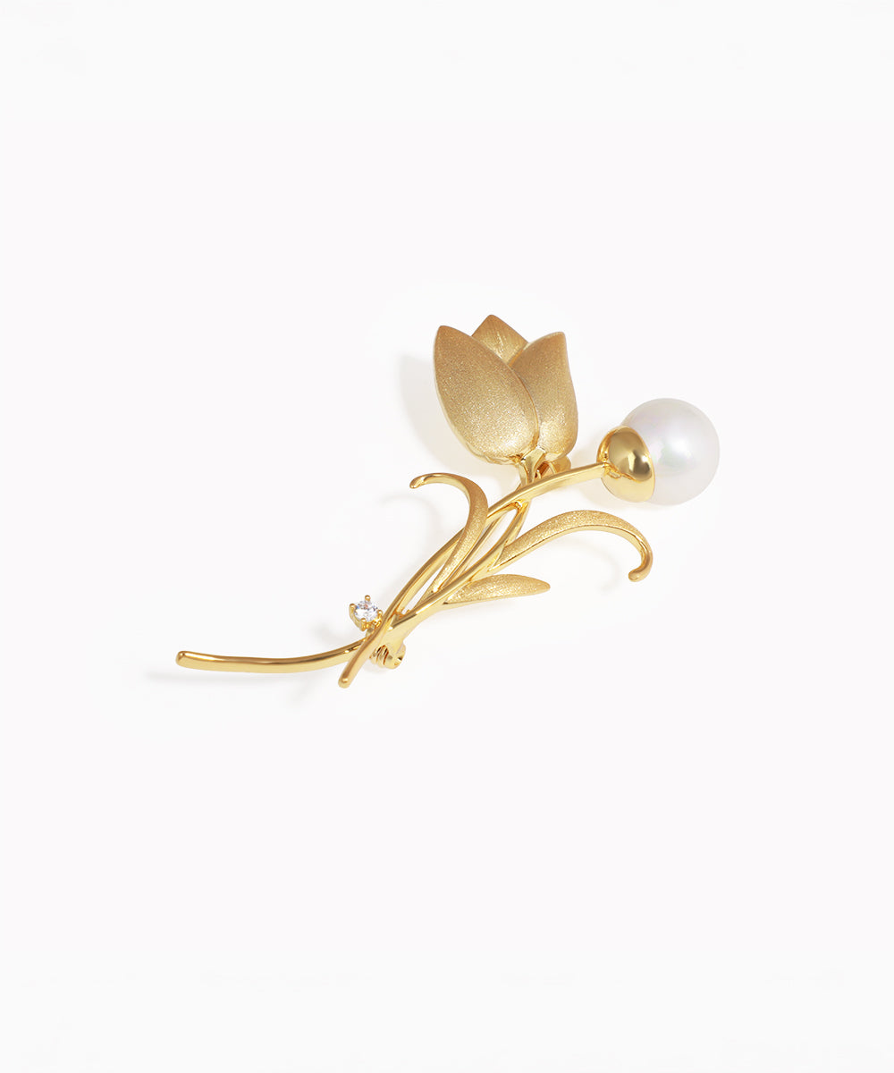 Gold tulip-shaped brooch with a pearl on a white background