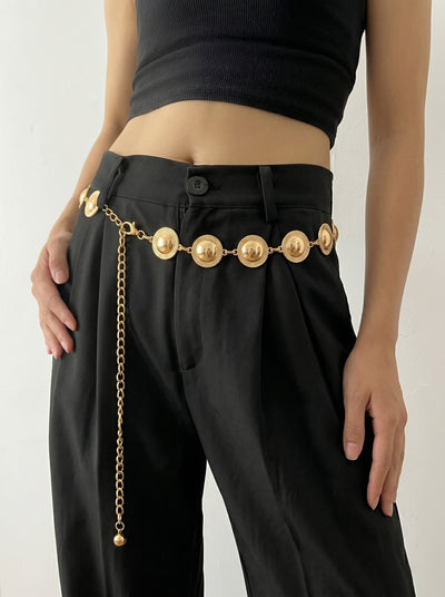 Person wearing black pants with a gold chain belt on a plain background