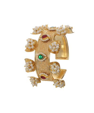 Gold-tone cuff bracelet with intricate engraving, pearl clusters, and red and green glass stones.