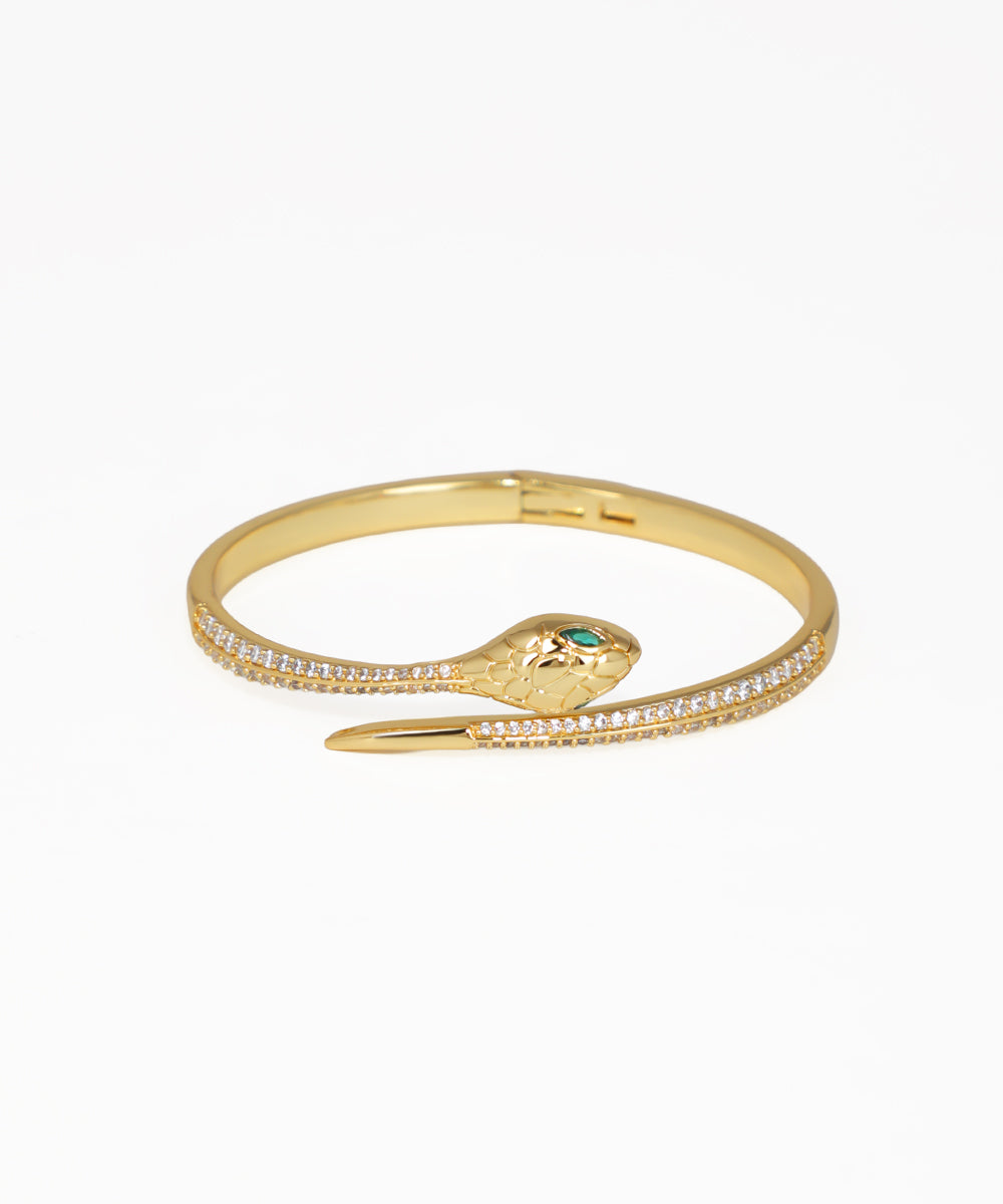 Gold-tone bangle kada with coiled serpent design, clear paved accents, and green eyes