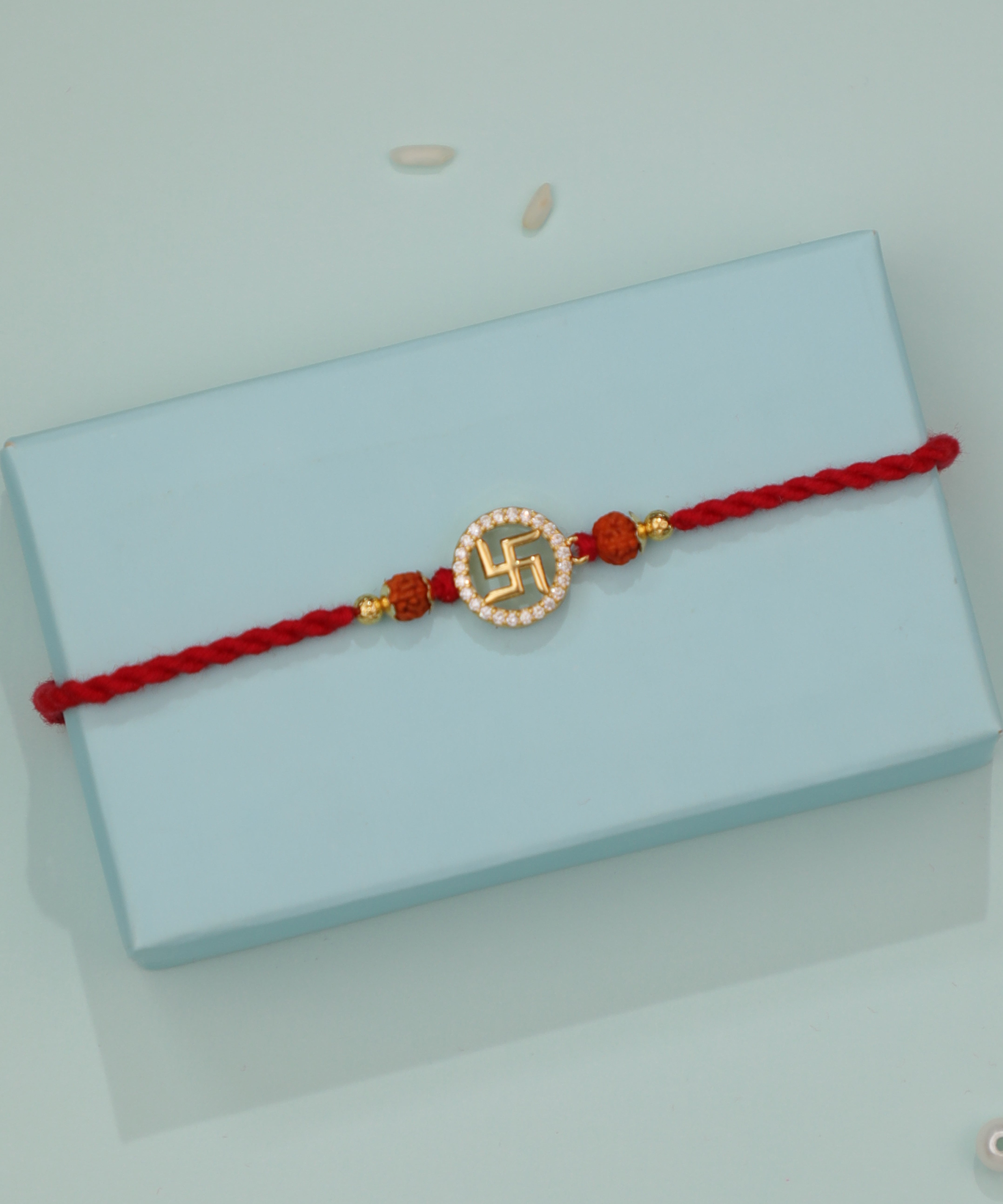 Gold-tone Rakhi with Swastika design, clear stones, and rudraksha beads on a red thread