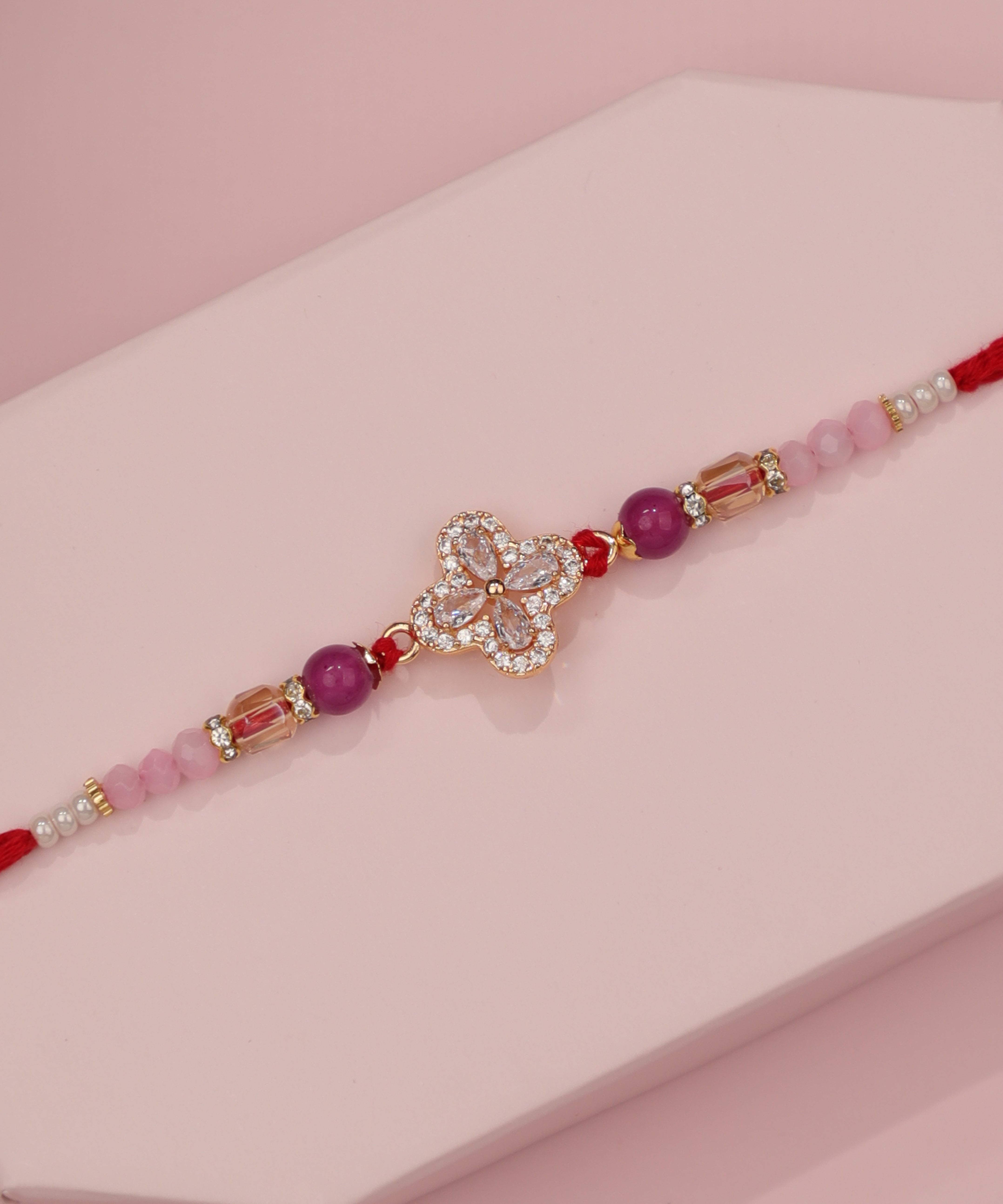 Gold-tone Rakhi with sparkling clover motif, purple and pink beads, and red thread ties.