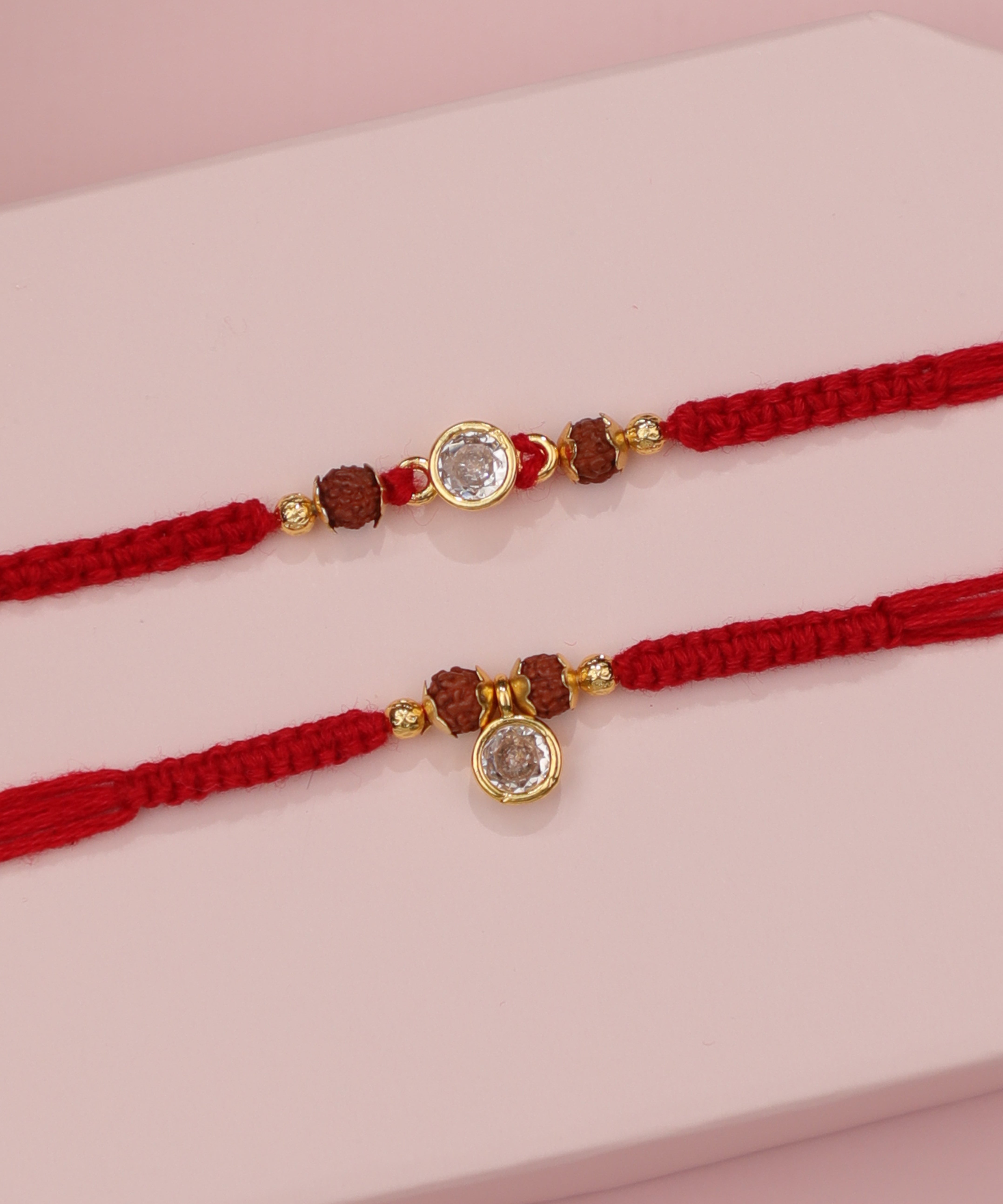 Gold-tone Rakhi with rudraksha beads and clear circular and drop stones on red thread
