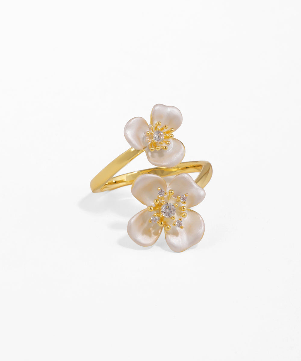 Gold ring with white floral designs on a light beige background