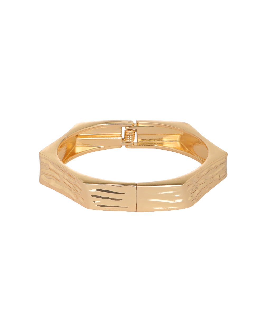 A gold-plated metal cuff bracelet with a textured, wavy pattern on the front and a polished finish, shown against a plain white background.