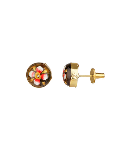 A pair of gold stud earrings featuring a circular black enamel face decorated with a hand-painted floral motif in pink, white, and yellow, shown against a plain white background.