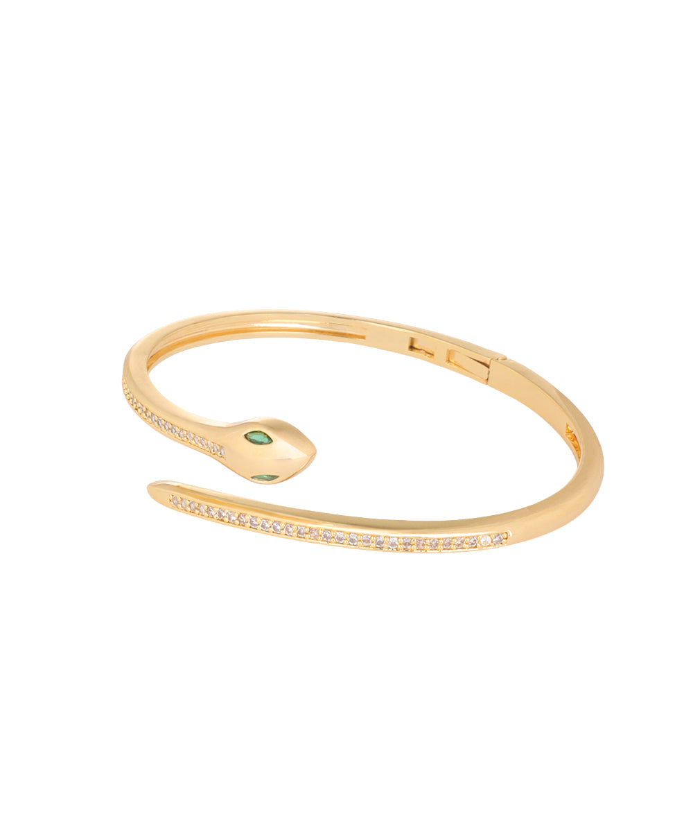 A gold snake-shaped cuff bracelet with a small green gemstone on its head and rows of clear pavé stones along the body, shown on a plain white background.
